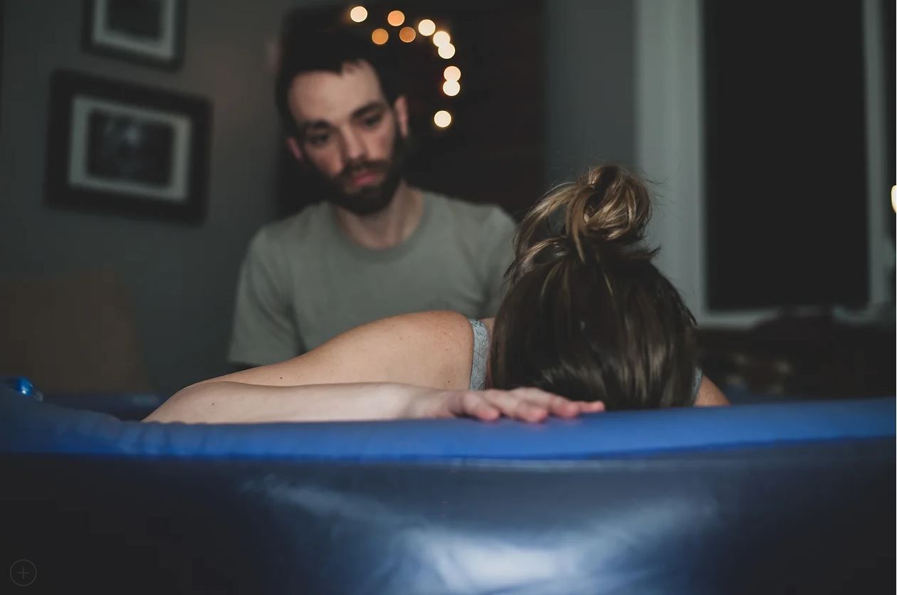 A home birth setting with a blue birthing pool in low ambient lighting.