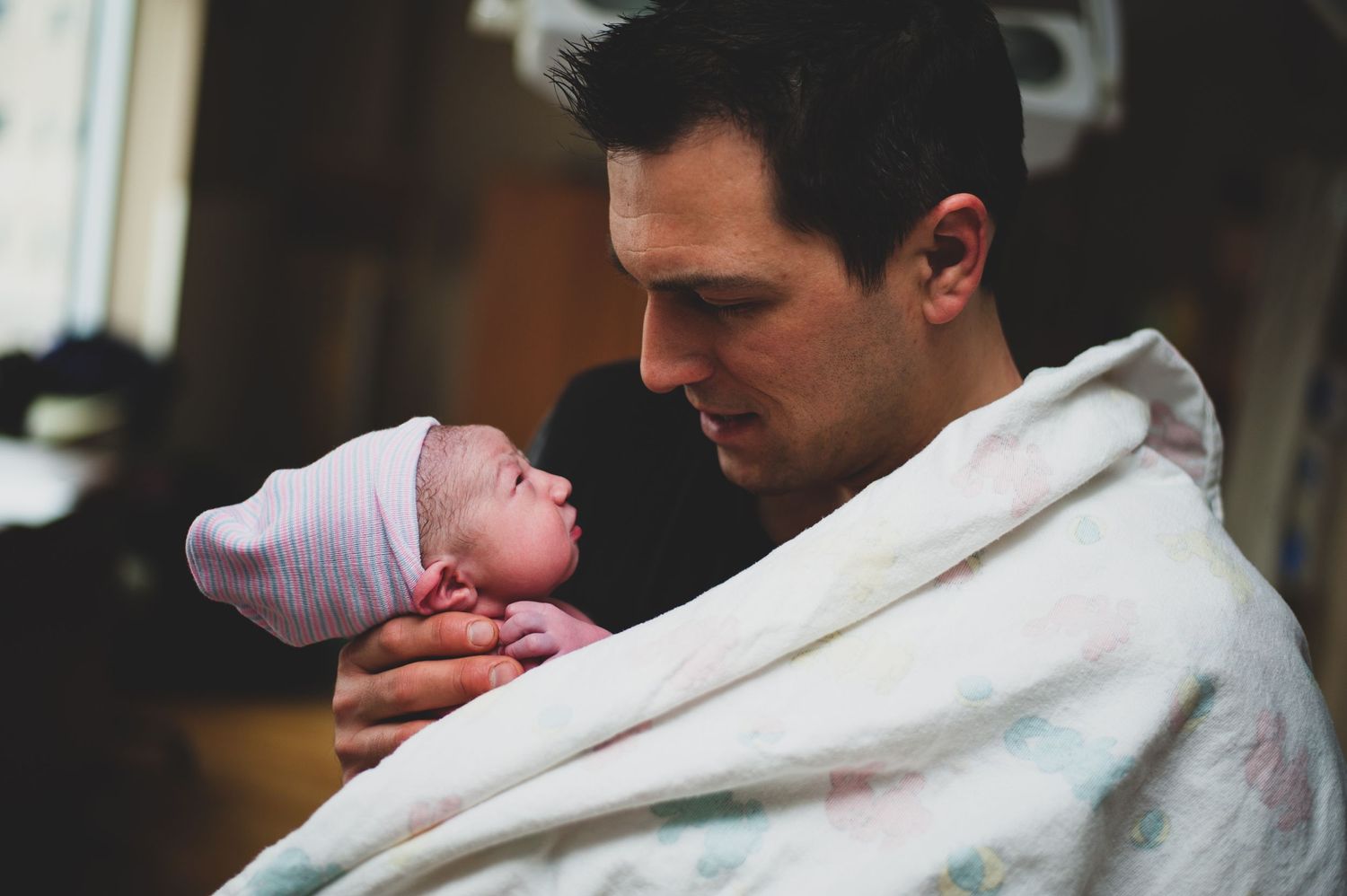 A newborn baby wrapped in a blanket being cradled gently in the delivery room.