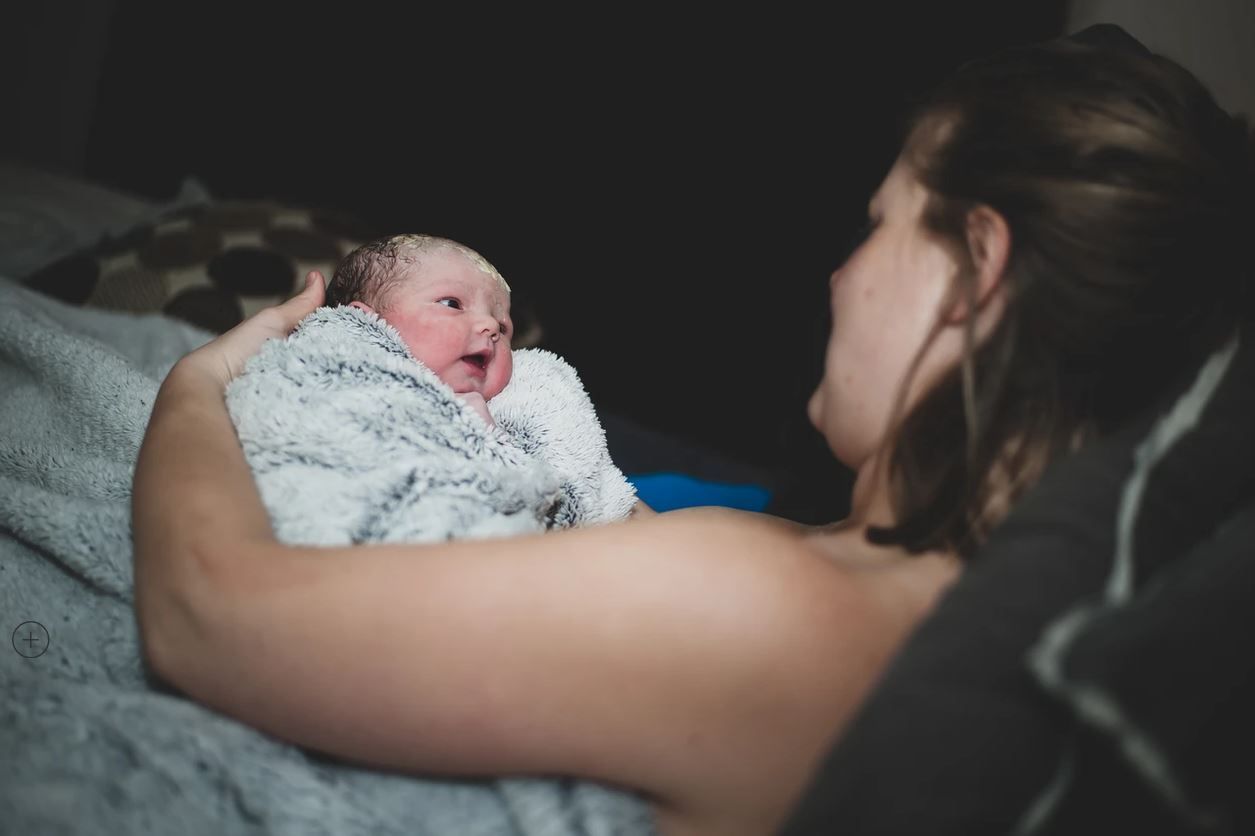 Newborn baby wrapped in white blanket being held and admired.
