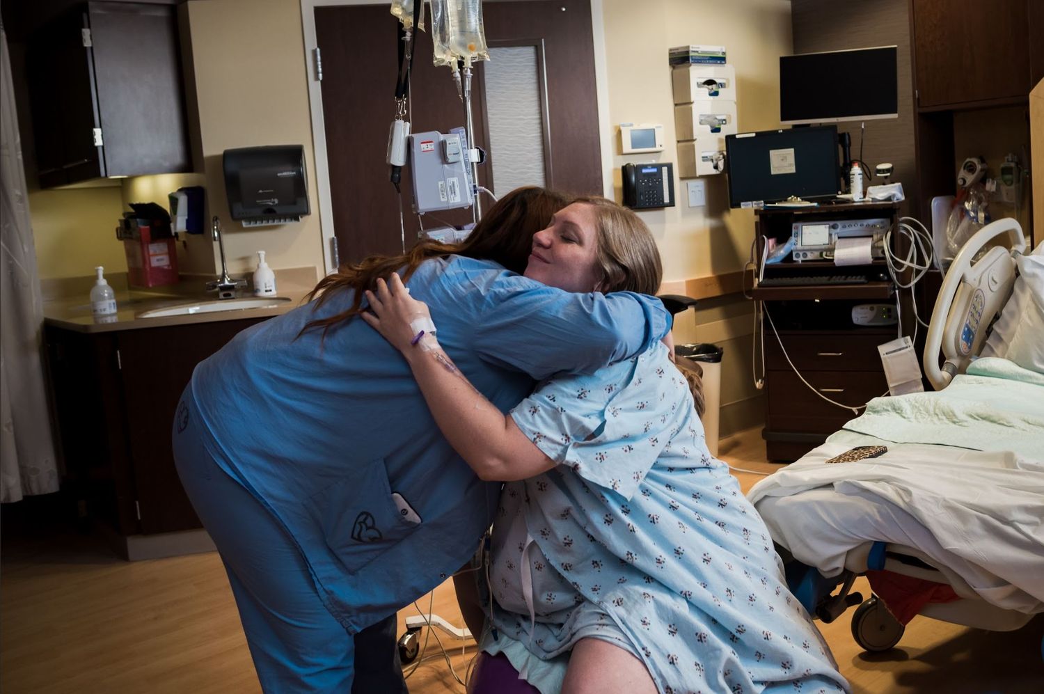 Labor nurse comforting laboring patient in hospital room with medical equipment visible.