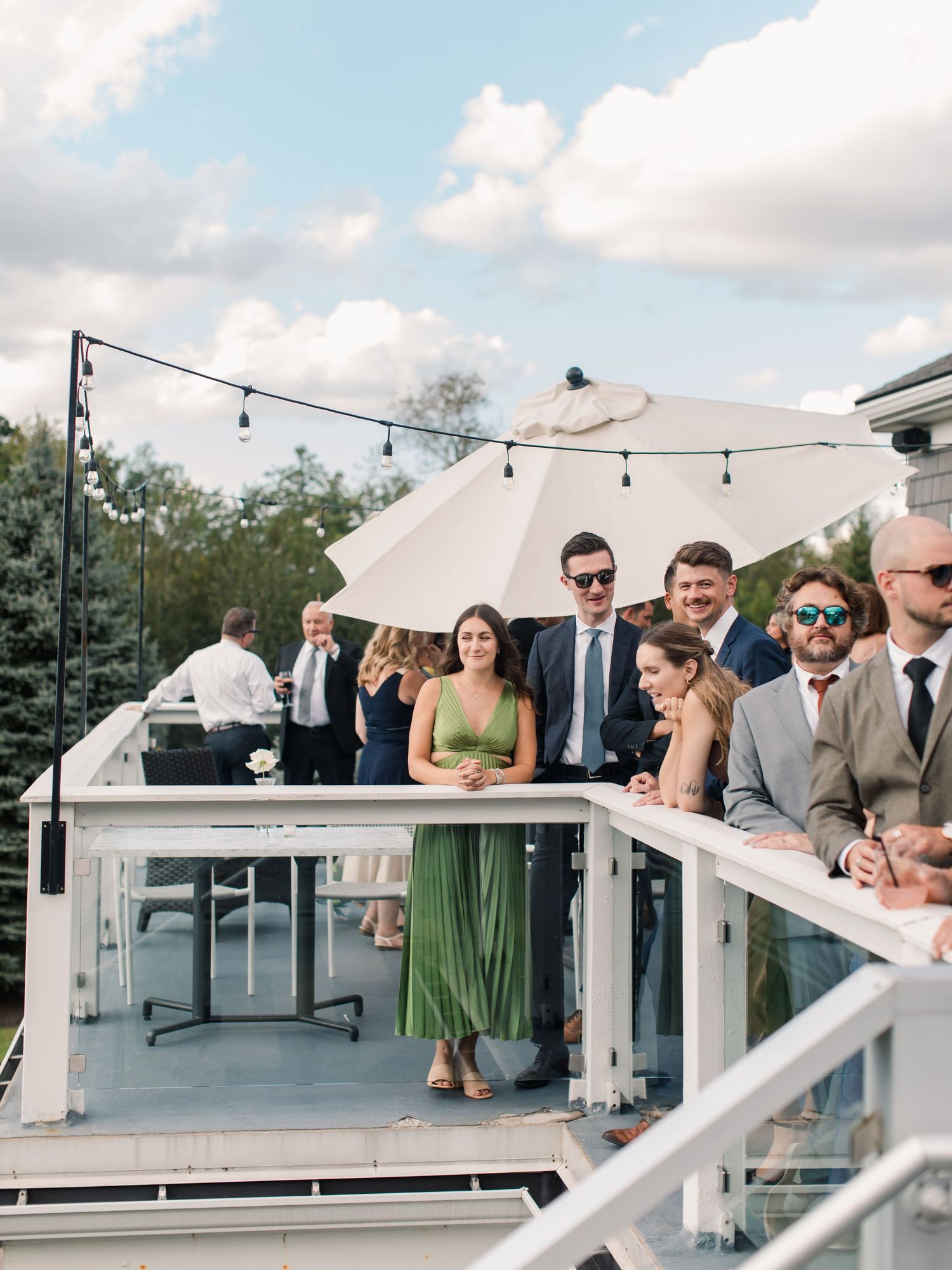 Elegant outdoor wedding reception table with gold chairs, white linens, and blue napkins set on a patio surrounded by lush greenery.
