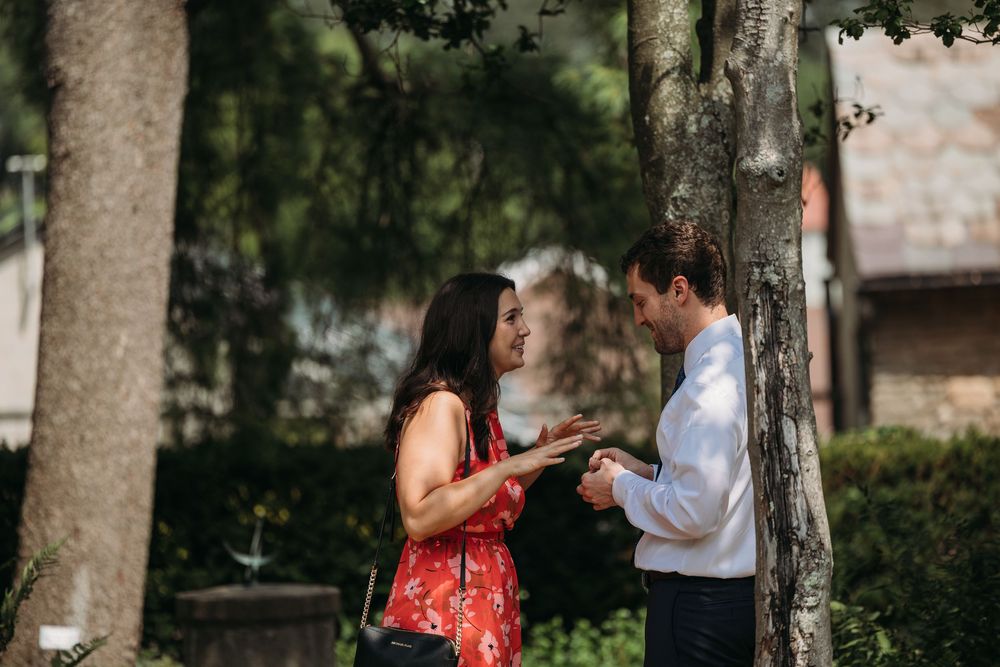 Couple sharing a romantic moment beside a tree in a lush garden, woman in red dress smiling.
