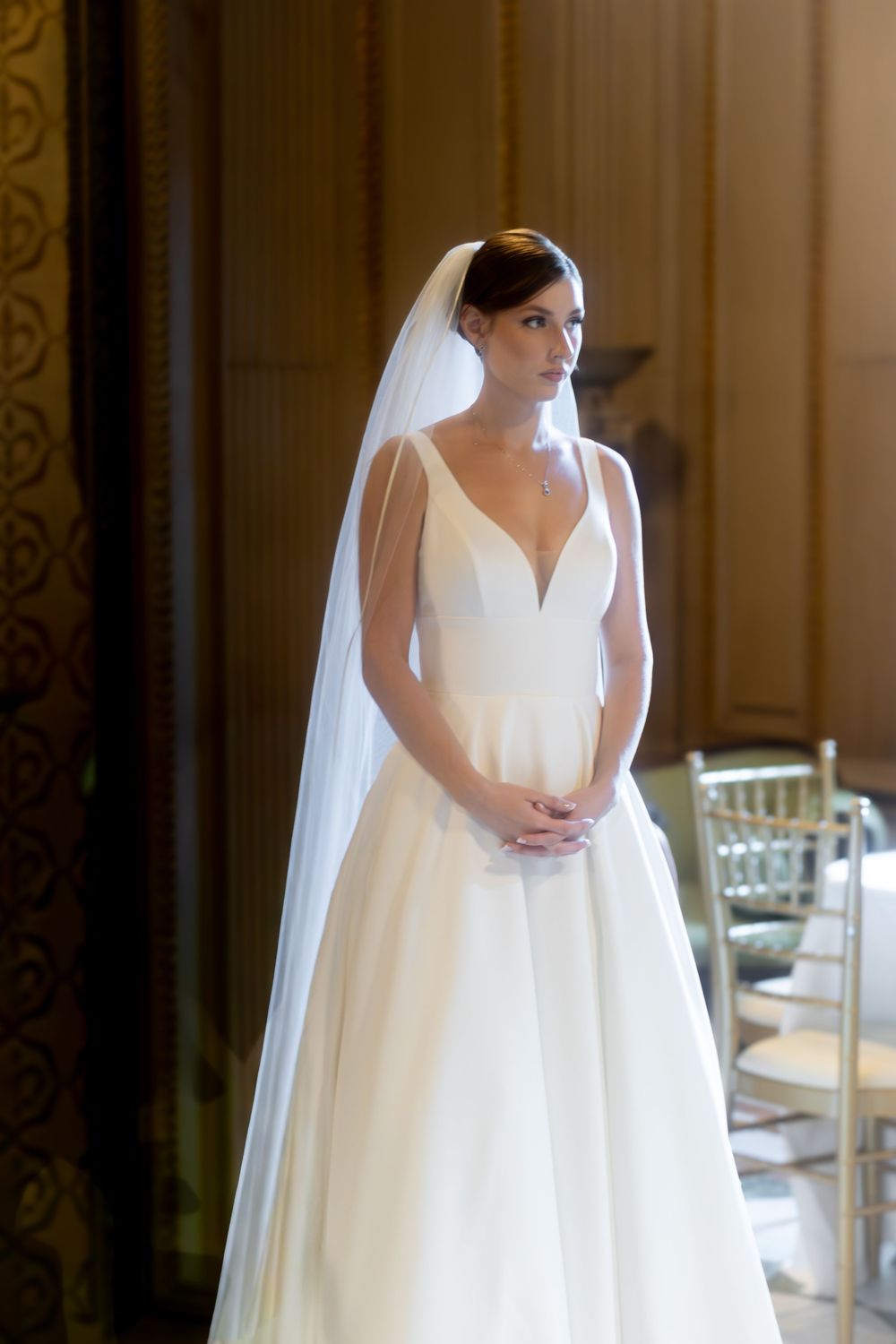 Elegant bride in a white ball gown with deep V-neckline and long veil standing in a grand venue.