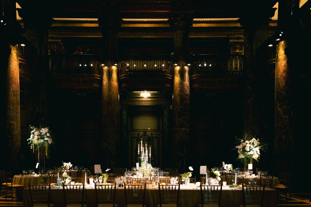 Elegant wedding reception in a grand ballroom with candlelit tables, floral centerpieces, and warm ambient lighting.