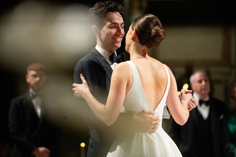 Couple sharing their first dance at a wedding reception, groom in tuxedo embracing bride in backless white gown.