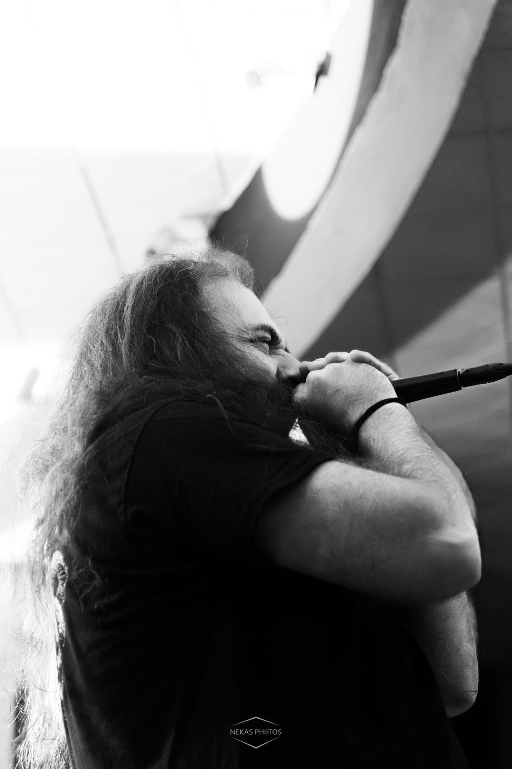 Black and white photo of a long-haired male vocalist performing on stage, singing intensely into a microphone.