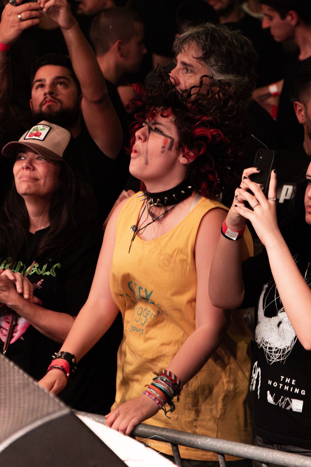 Excited concert fan in yellow tank top and choker necklace enjoys live music show in crowded venue.