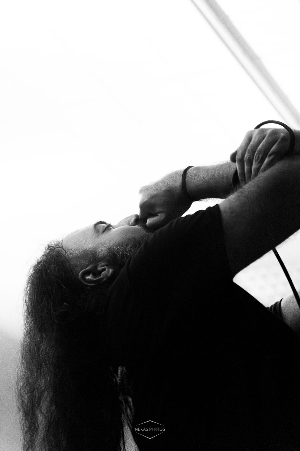 Black and white photo of a long-haired musician singing passionately into a microphone at a live concert.