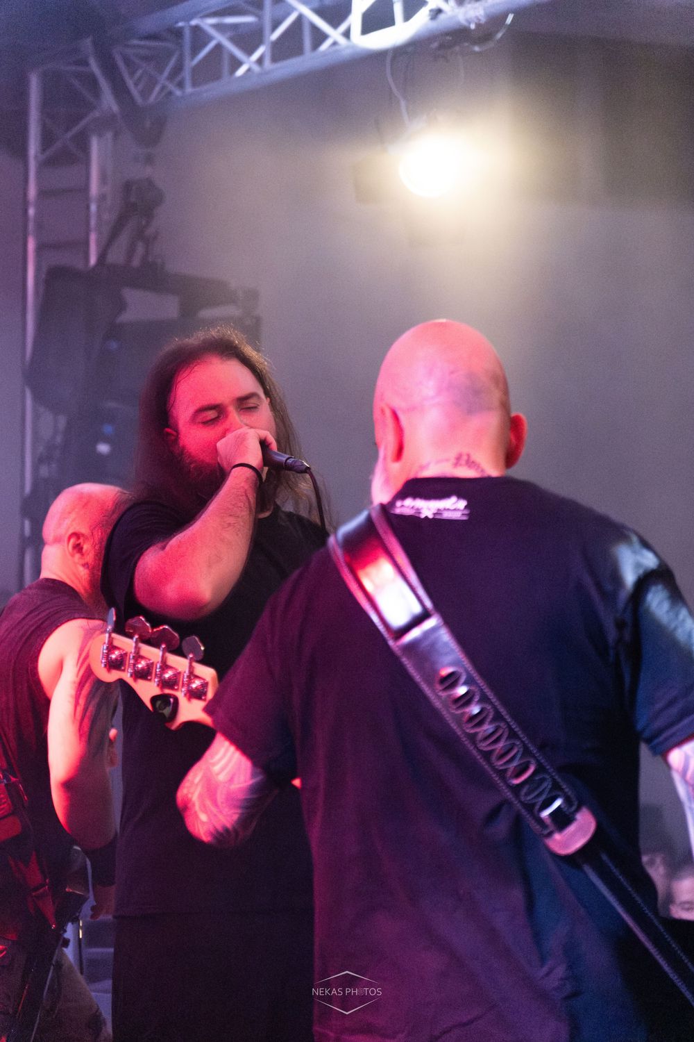 Heavy metal band performing live on stage, guitarist and long-haired vocalist singing into microphone under dramatic lighting.