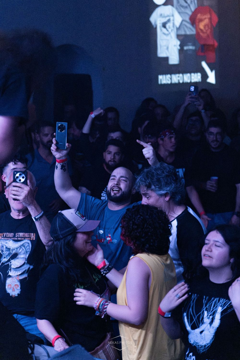 Excited concert crowd with fans holding up phones to record live music event at a dark venue.
