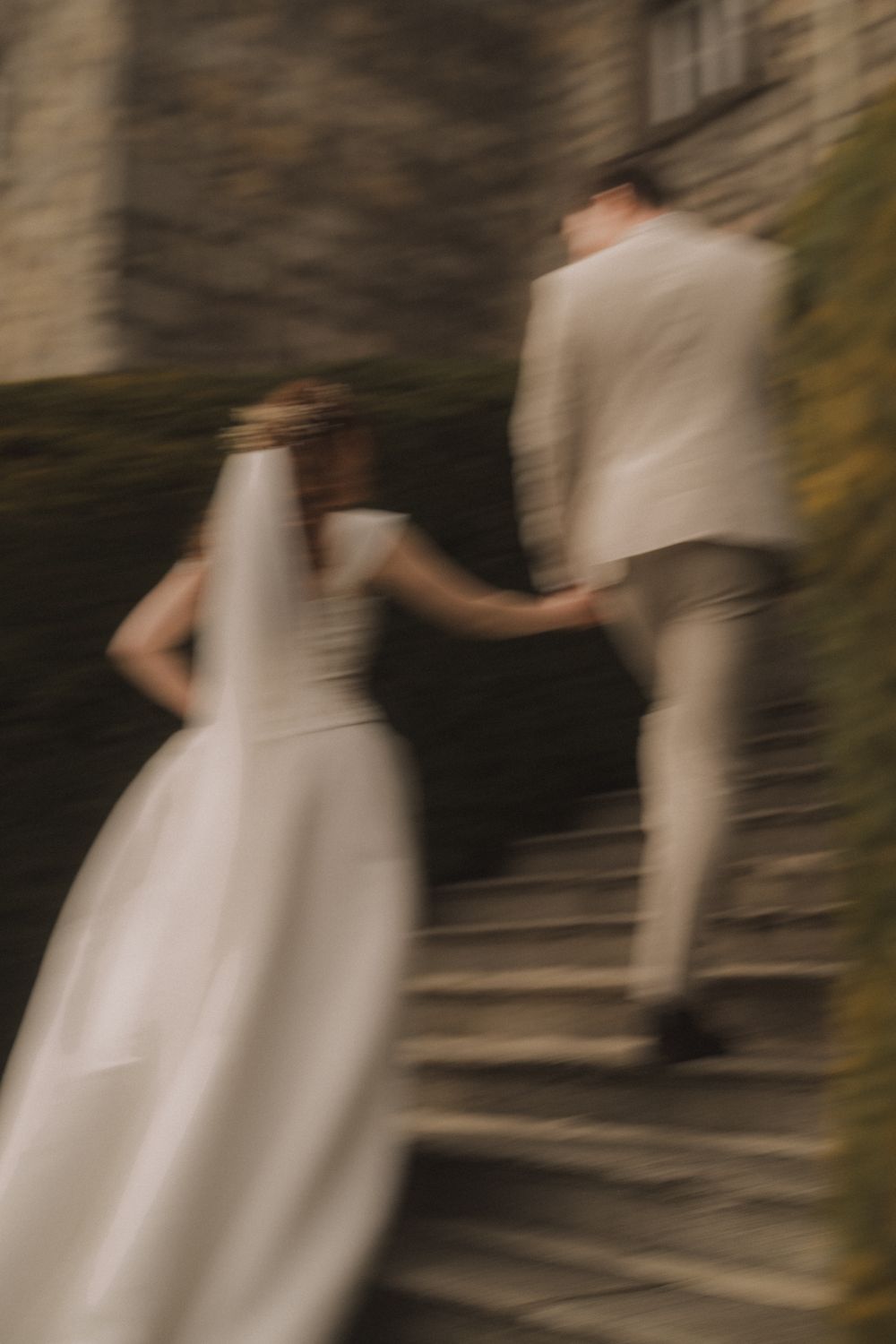 Blurred motion shot of bride and groom holding hands walking up stone steps on their wedding day.