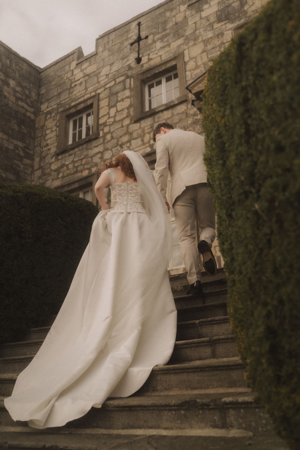 Bride and groom walking up stone steps toward a historic stone building on their wedding day.