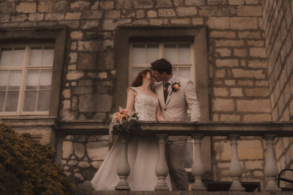 Bride and groom share a romantic kiss on a stone balcony of a historic castle venue on their wedding day.