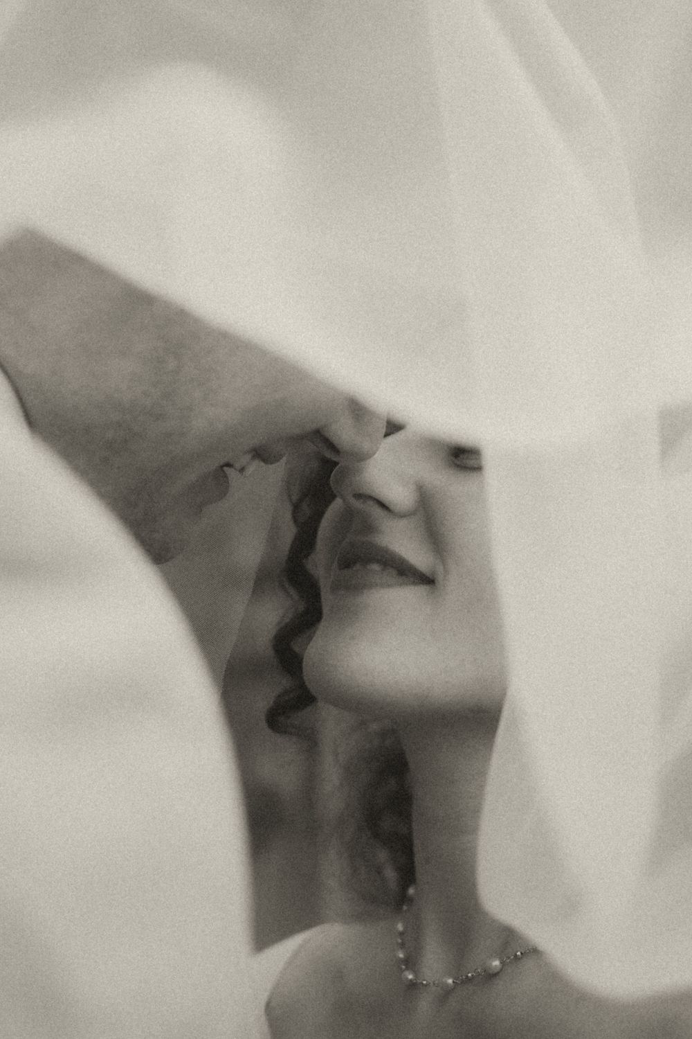 Black and white photo of a bride and groom sharing a romantic kiss beneath a flowing white wedding veil.