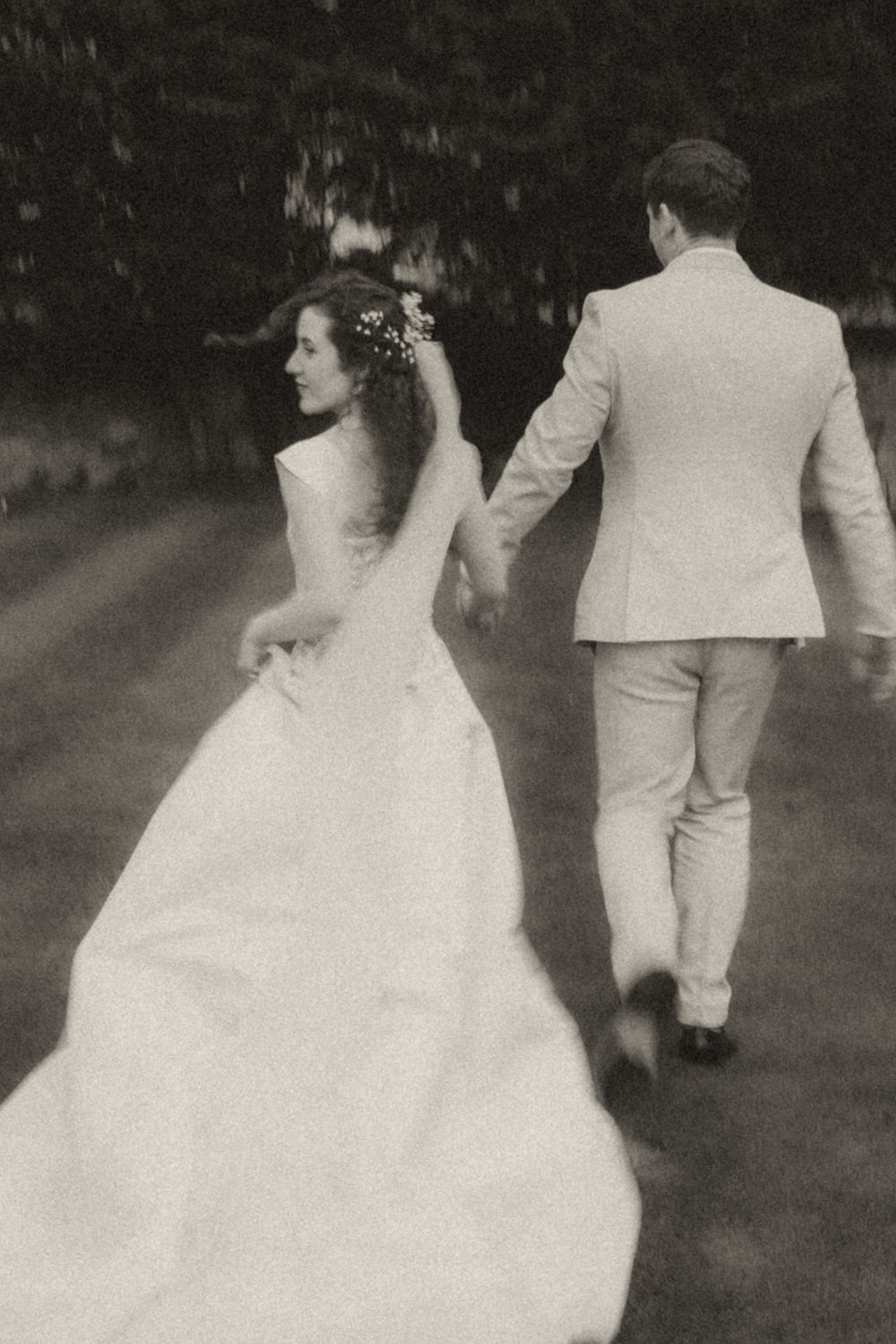 Black and white photo of bride and groom holding hands walking outdoors on their wedding day.