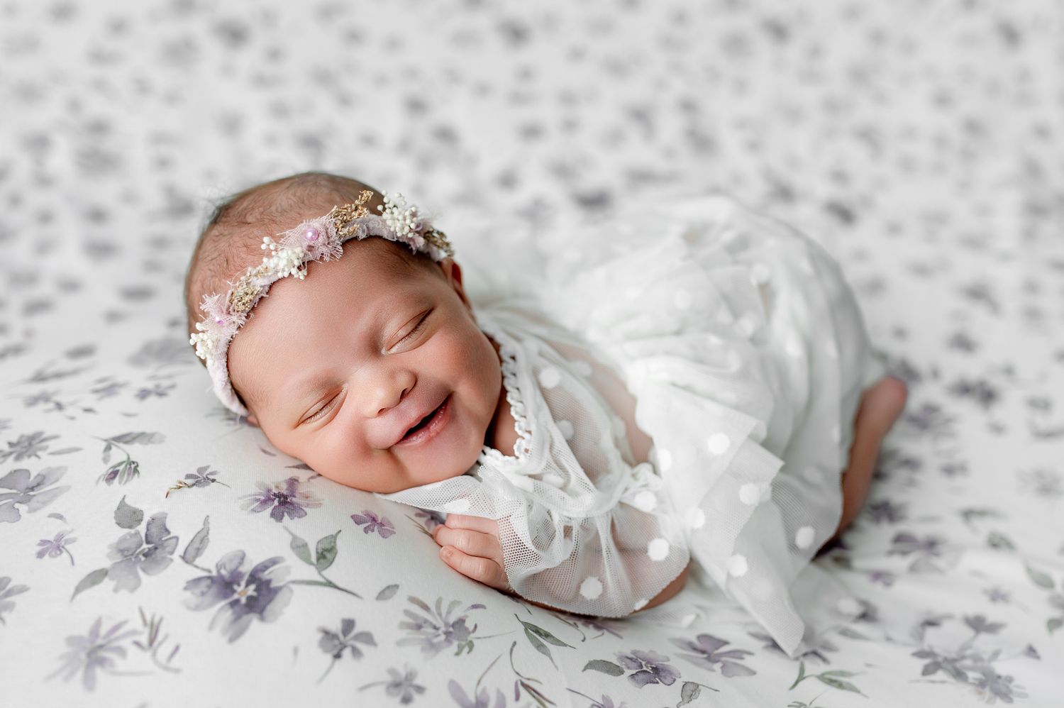 Sleeping newborn baby in olive green romper with fists raised, posed on matching green backdrop.