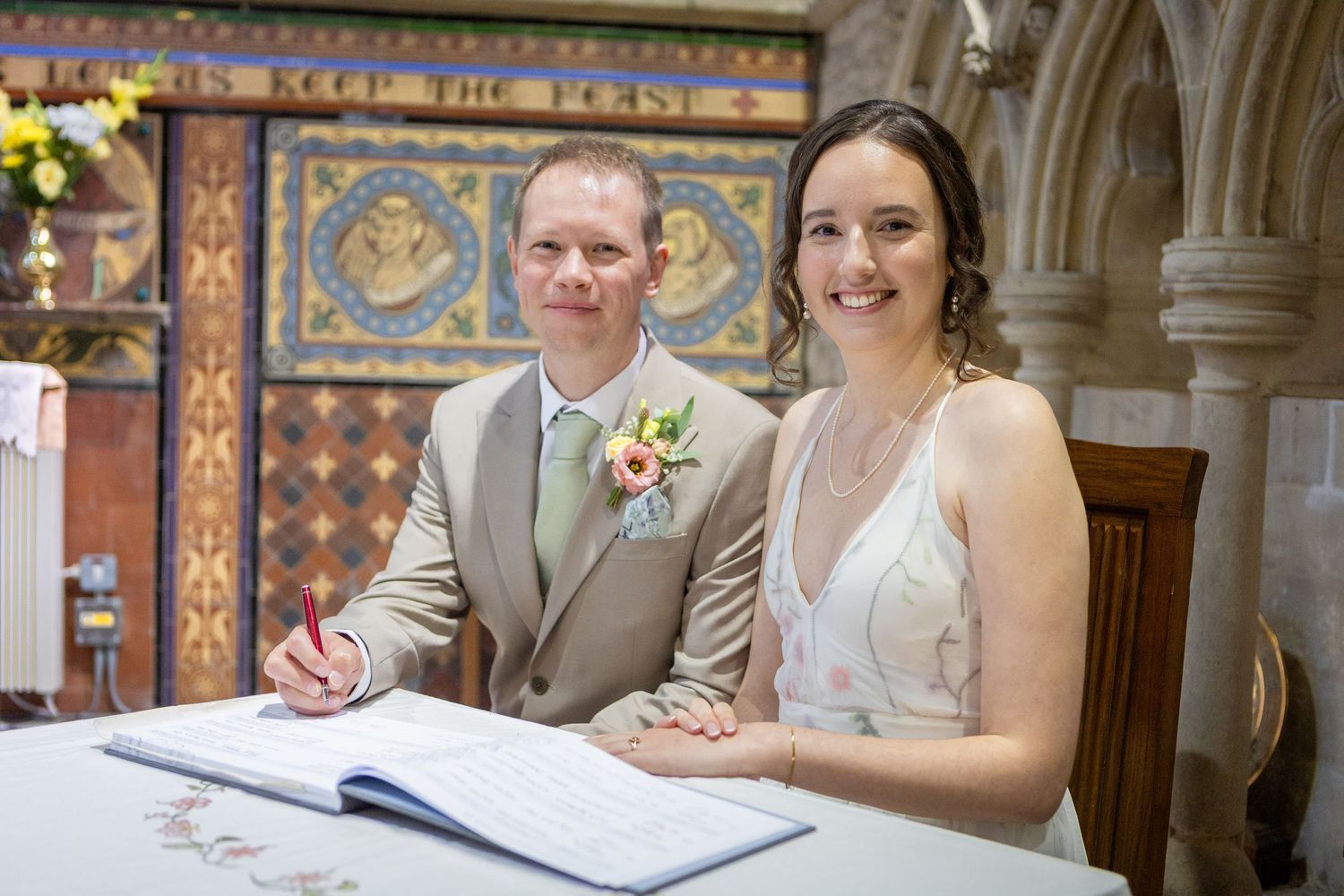 Bride and groom smiling while signing the wedding register inside a decorated church.