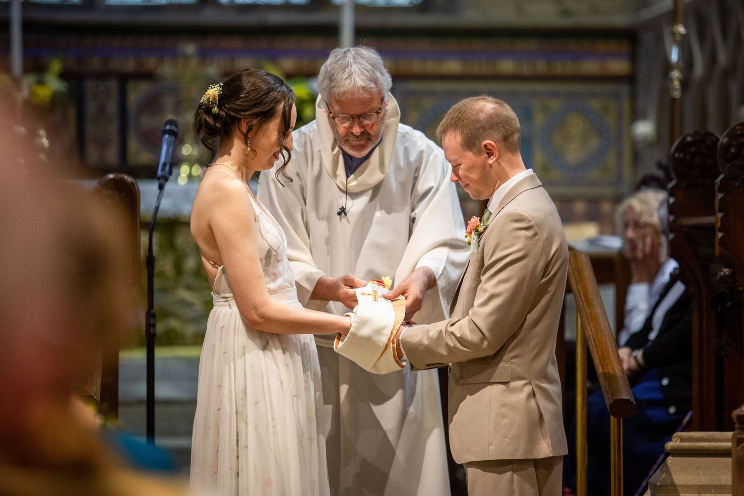 Priest officiating wedding ceremony as bride and groom exchange vows inside an ornate church.