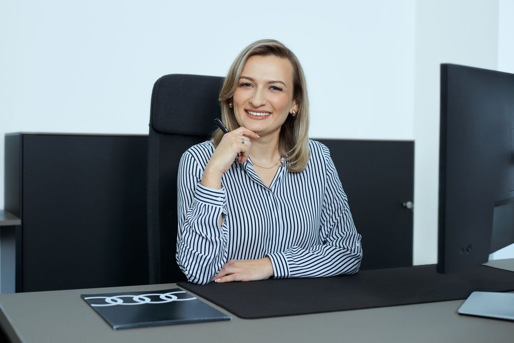 Professional businesswoman smiling at desk with computer monitors in modern office setting.