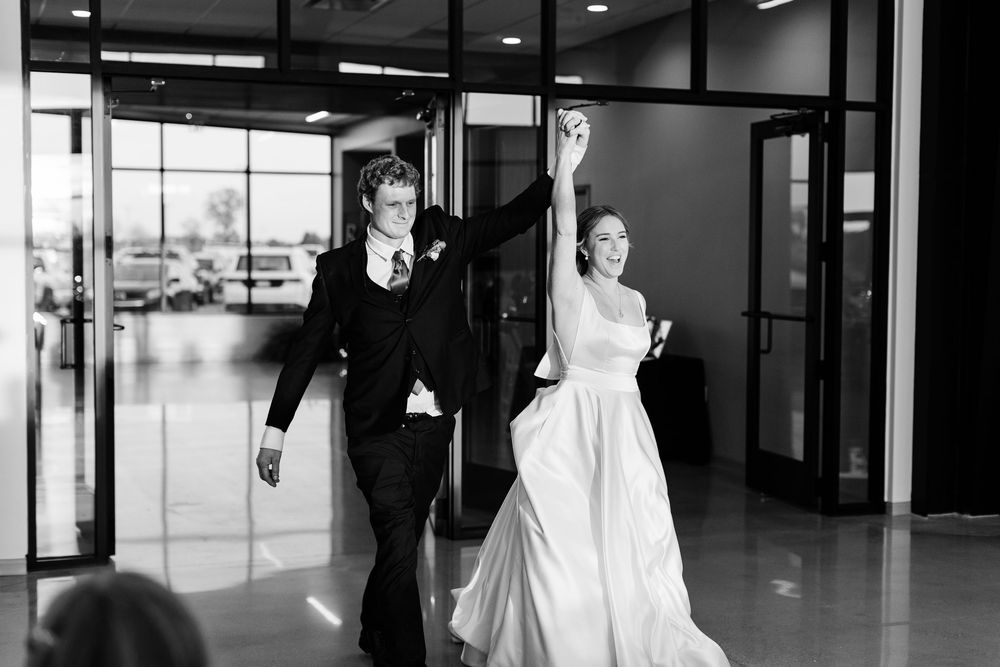 Black and white photo of a bride and groom making a grand entrance, bride raising her arm in celebration.