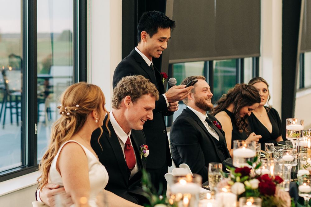 Wedding party seated at head table as best man delivers a heartfelt toast to the bride and groom.
