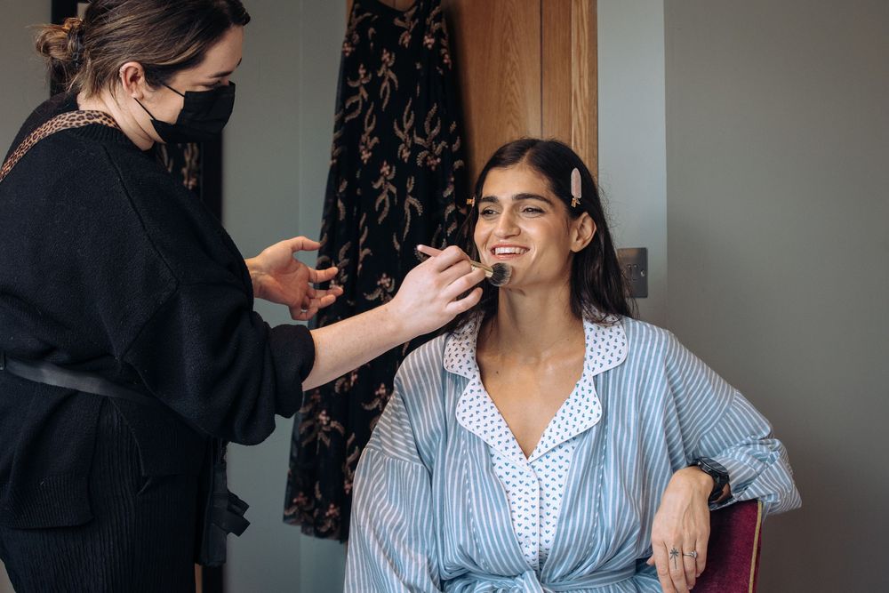 Makeup artist applying cosmetics to a woman in a striped blue shirt sitting in a salon chair.