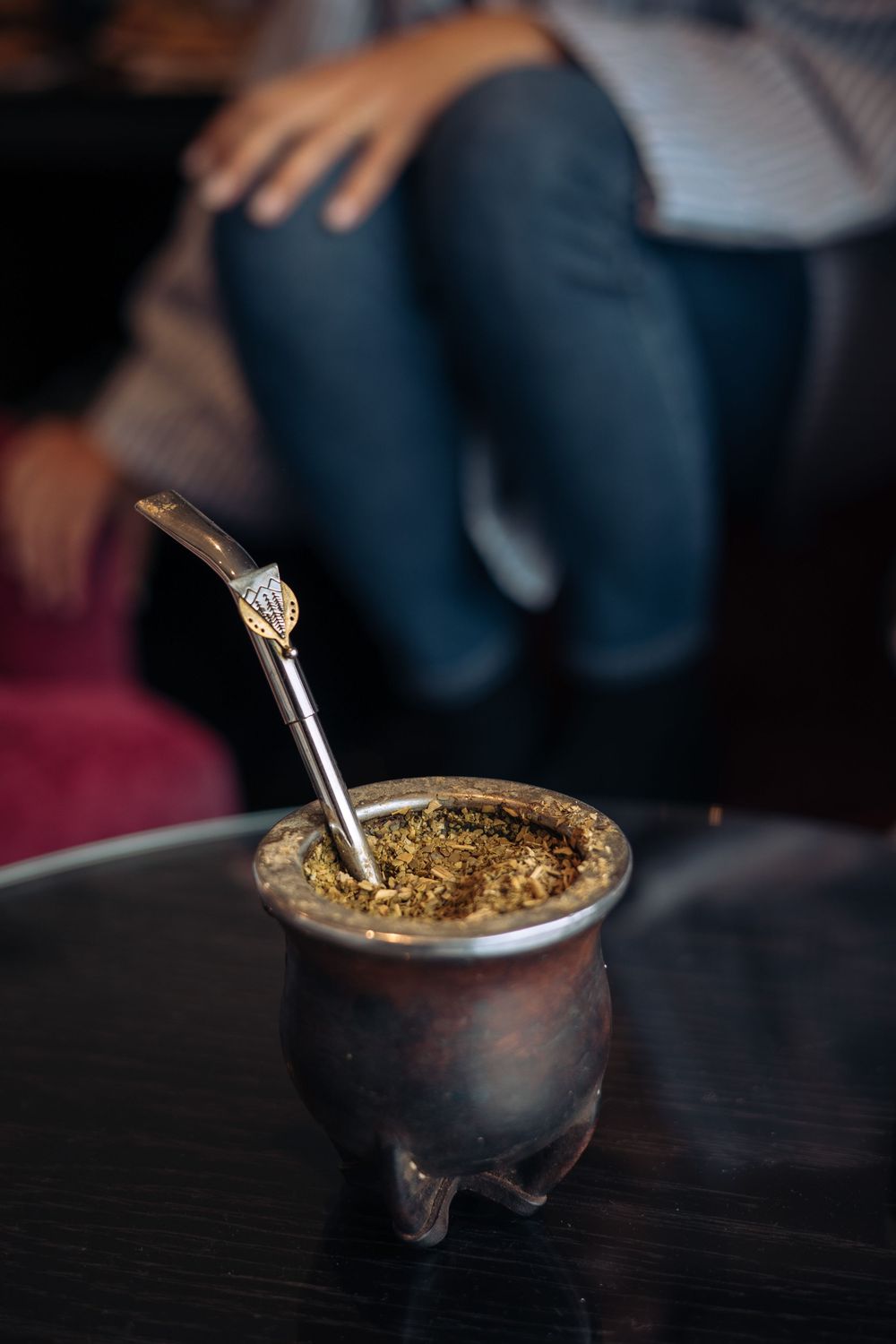 Traditional Argentine mate gourd with metal bombilla straw on dark table in cozy cafe setting.