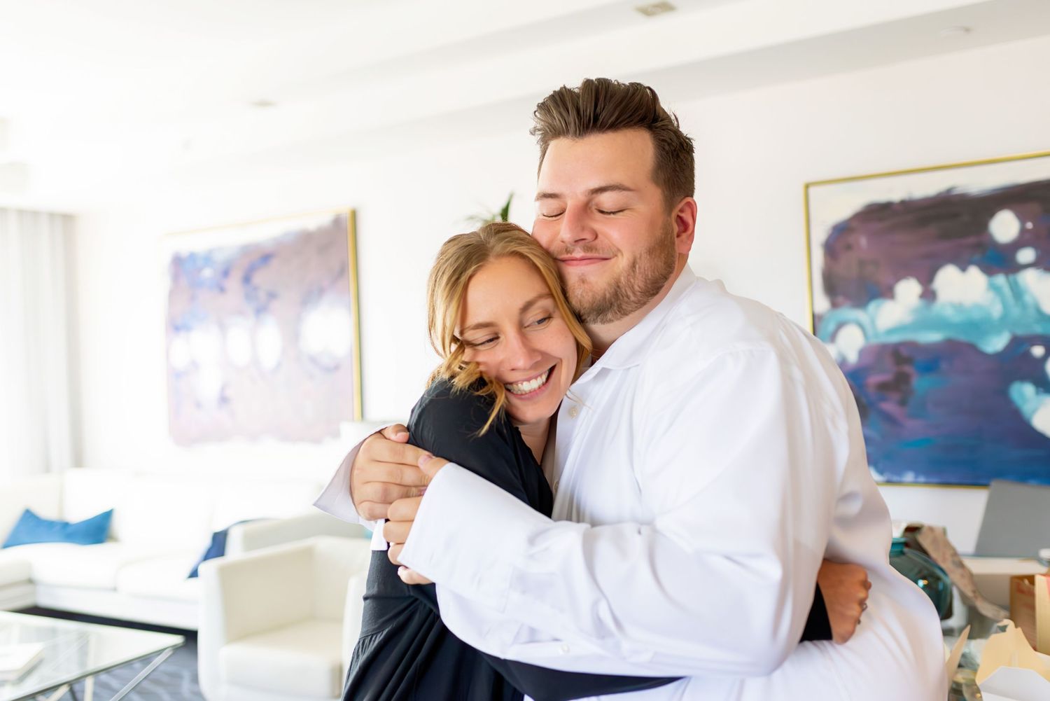 A happy couple sharing a warm hug in a bright modern living room with colorful abstract artwork on the walls.