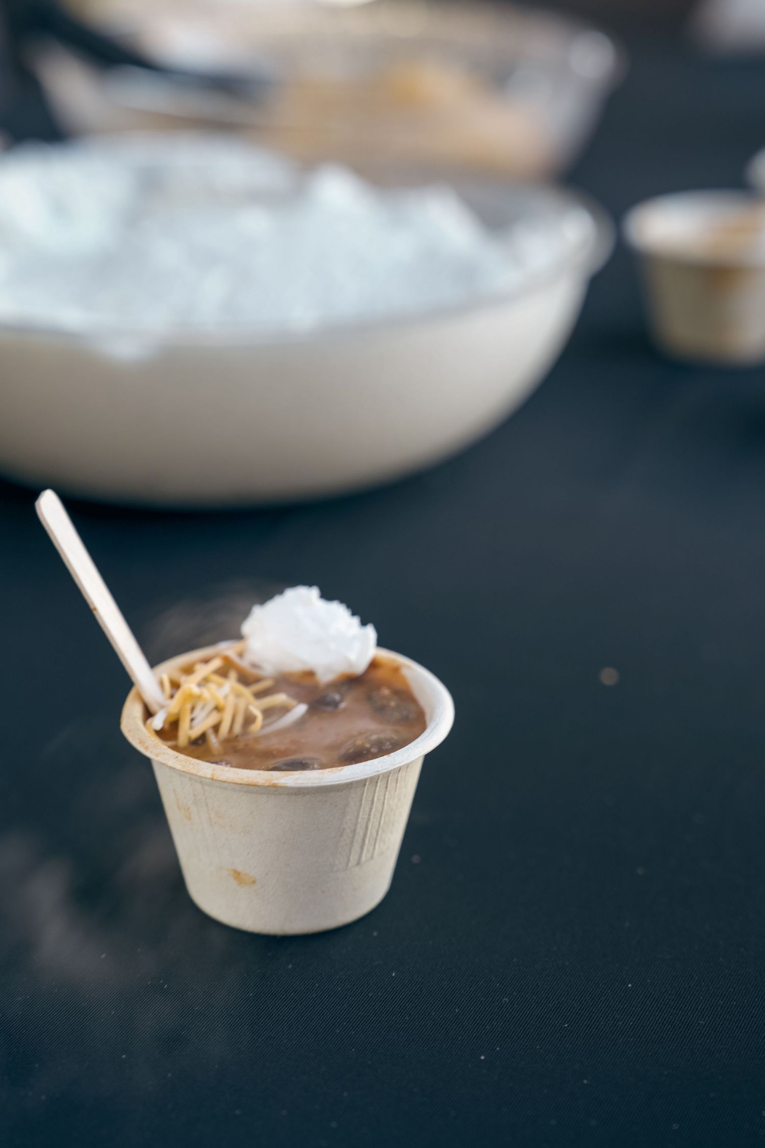 A small cup of chocolate pudding topped with whipped cream and shredded coconut at an outdoor event.