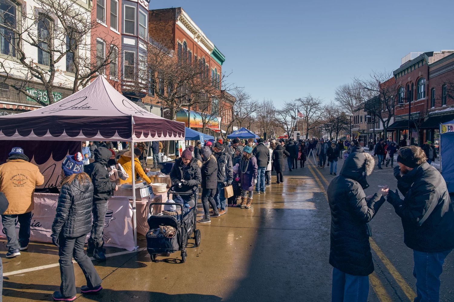 Crowds gather along busy street market lined with vendor tents on a cold winter day.