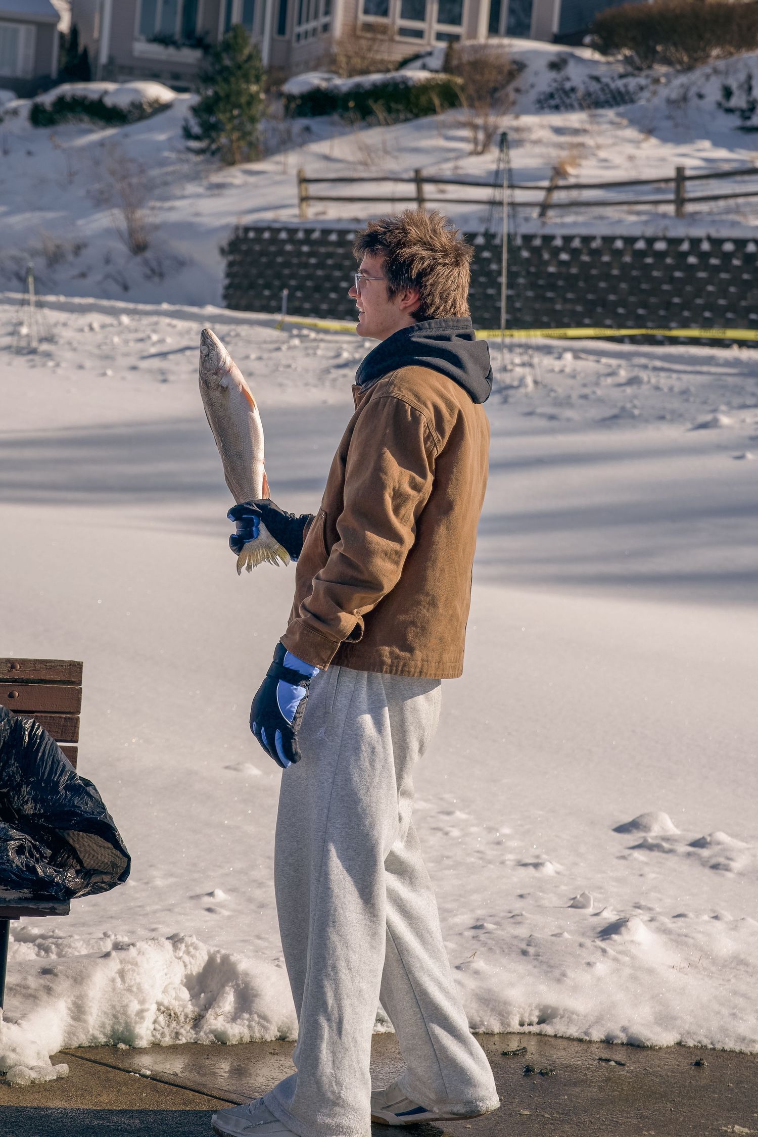 Man in brown jacket and gray sweatpants holding a large fish chunk outdoors in snowy winter conditions.