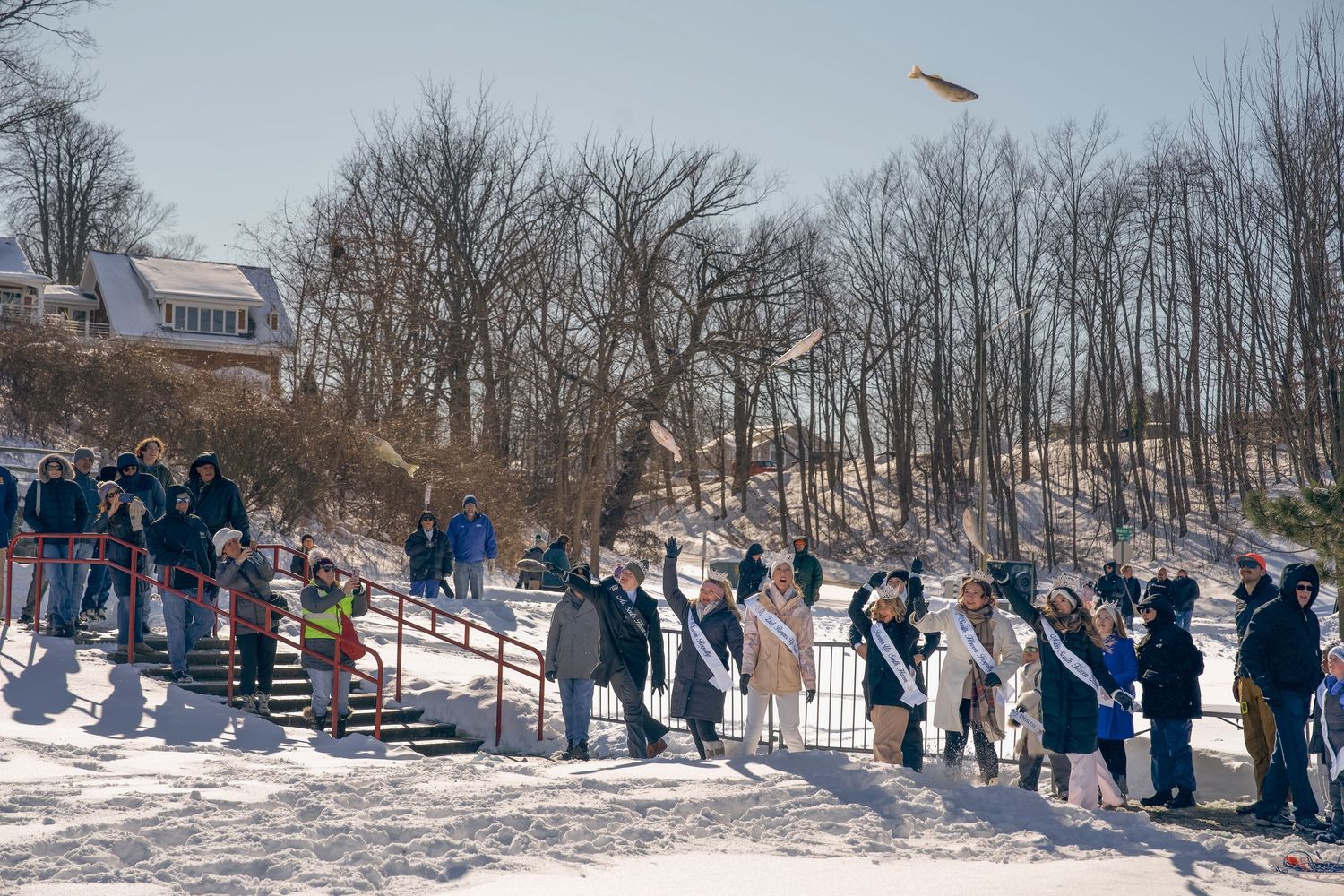 Crowd of people standing on a snowy hillside watching an outdoor winter event on a sunny day.
