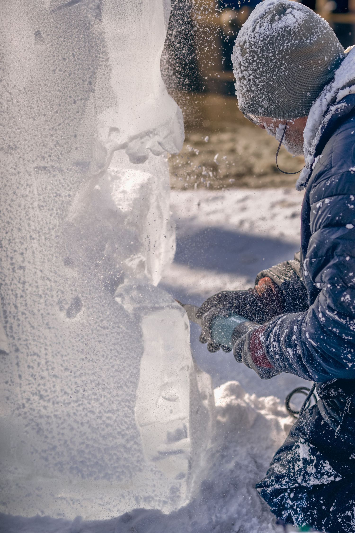 Artist carefully sculpts detailed ice sculpture using handheld tool in cold winter weather.