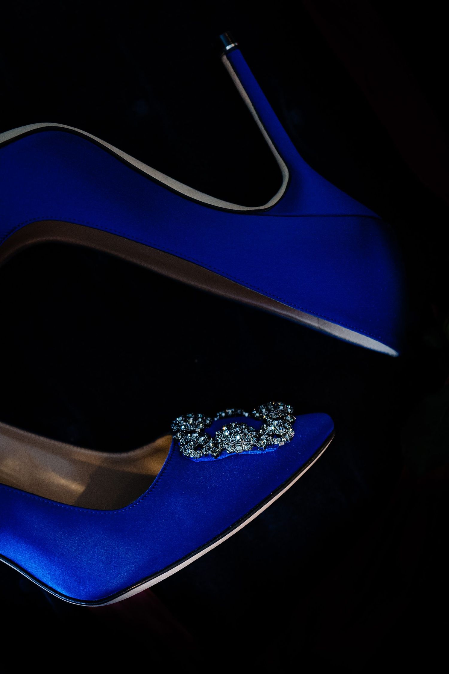 Elegant royal blue satin high heel pumps with crystal embellishment on black background.