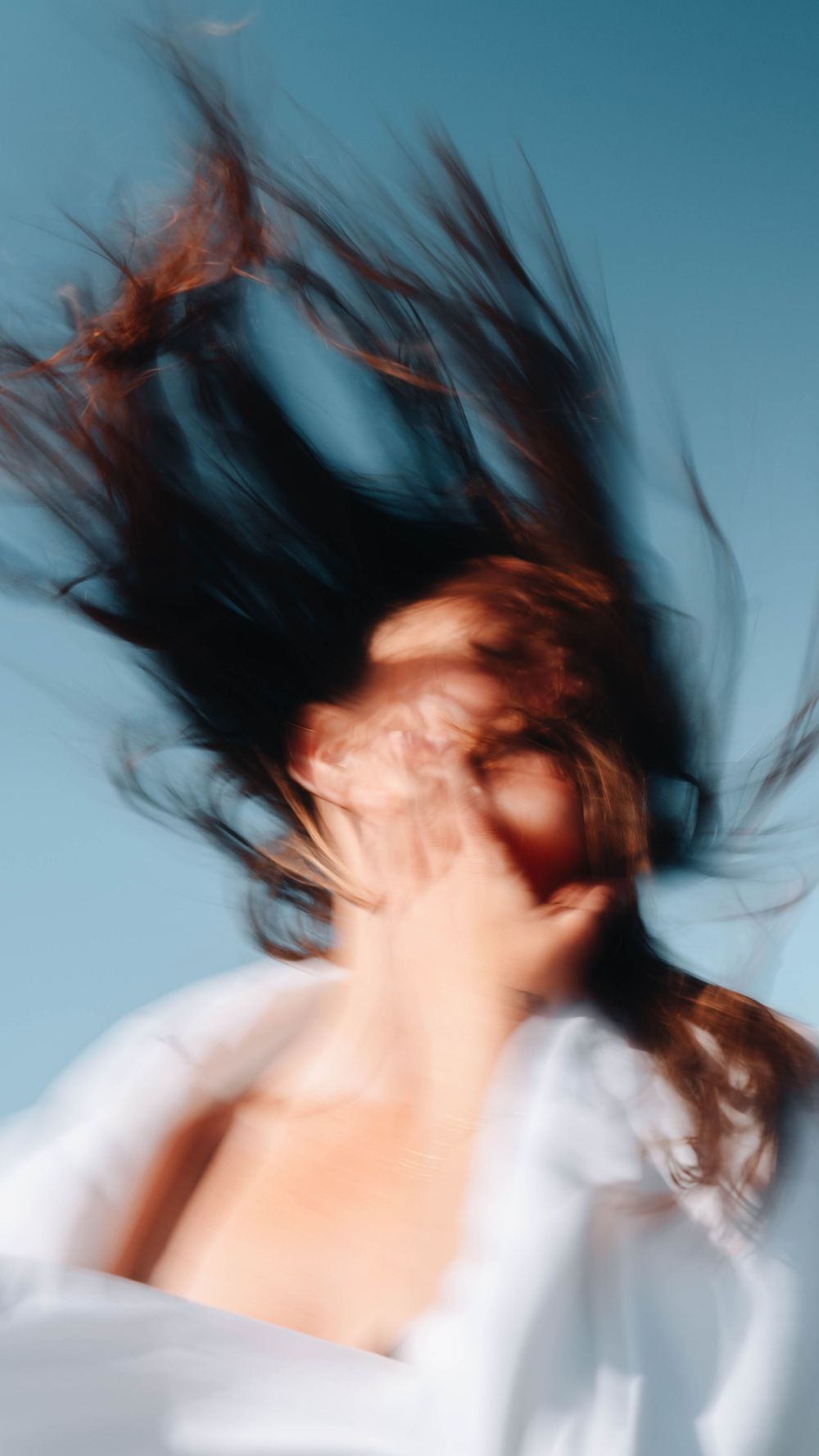 woman with wild hair in the wind long exposure caressing own face by the ocean in a moody exposure by the coast of NSW