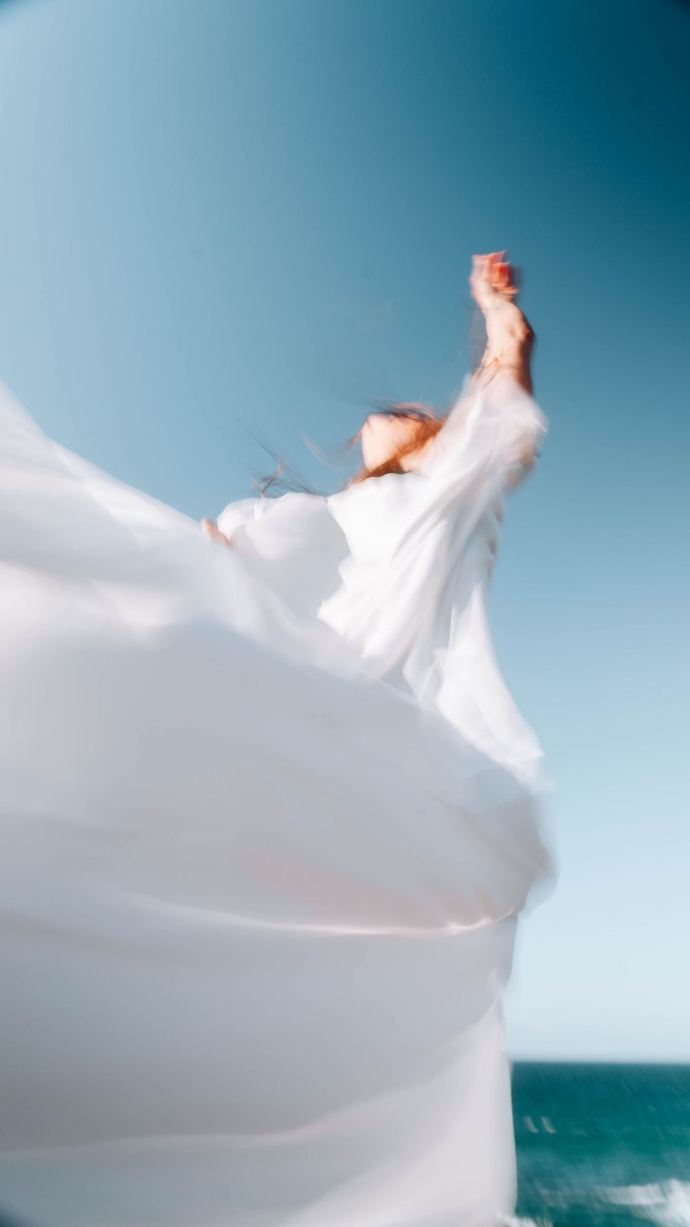 woman reaching into the sky in a freeing pose with the ocean in the background and veil in the wind in Newcastle NSW