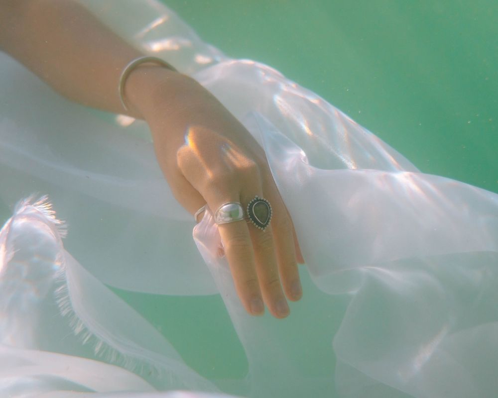 girl with jewellery rings and bangles underwater in a dream like tone with light shining through the ocean waves in Newcastle NSW
