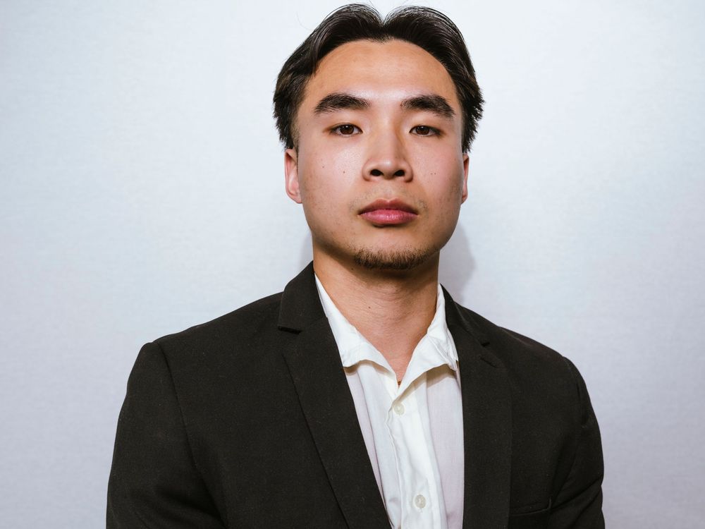 Young Asian man in black blazer and white dress shirt poses for professional headshot photo.