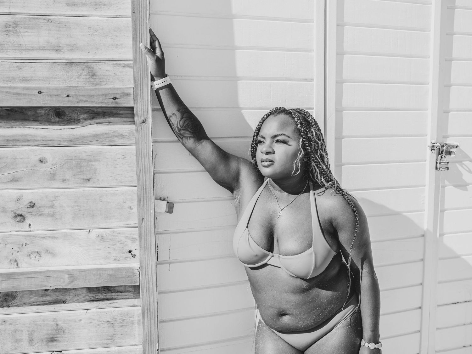 Black and white photo of a woman in a bikini posing confidently against a wooden wall outdoors.