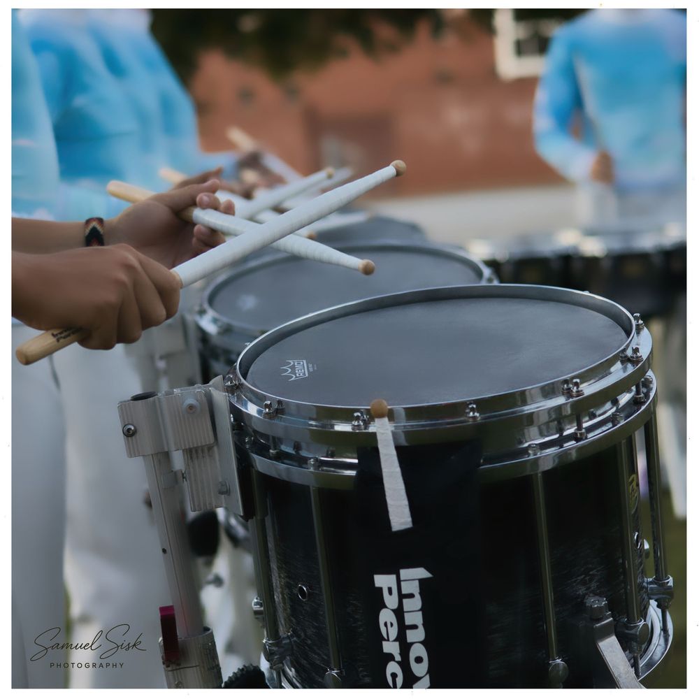 Close-up of marching band members playing snare drums during an outdoor performance.