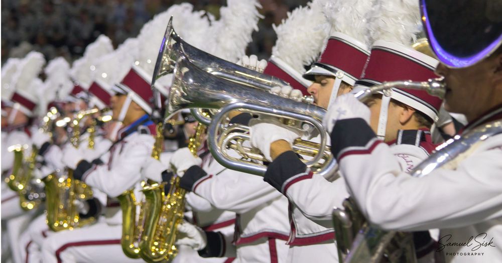 Marching band musicians in white and red uniforms playing brass instruments at night.