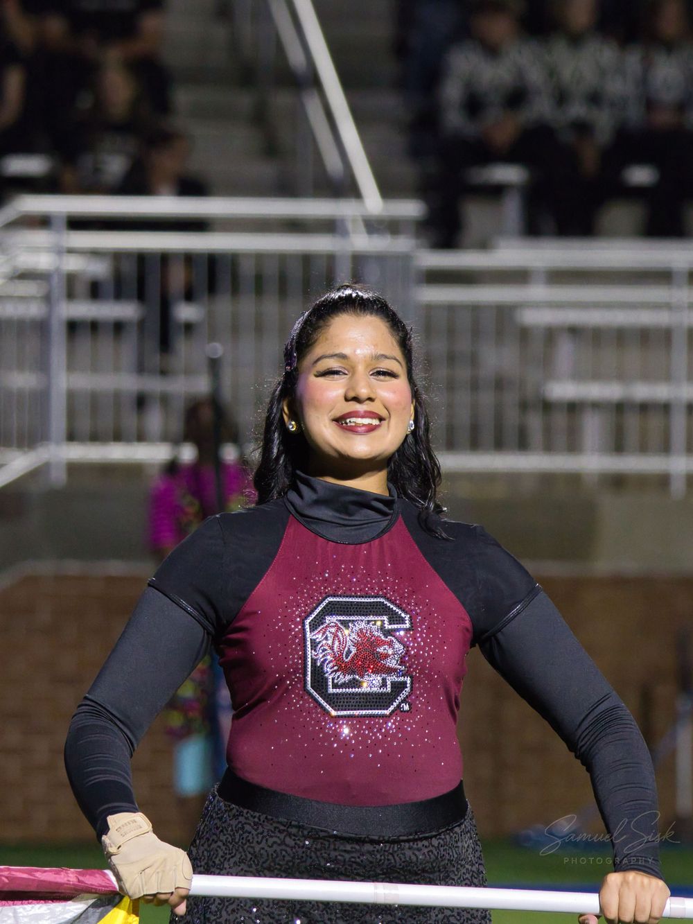 Smiling female marching band member in South Carolina Gamecocks uniform holding a flag pole.