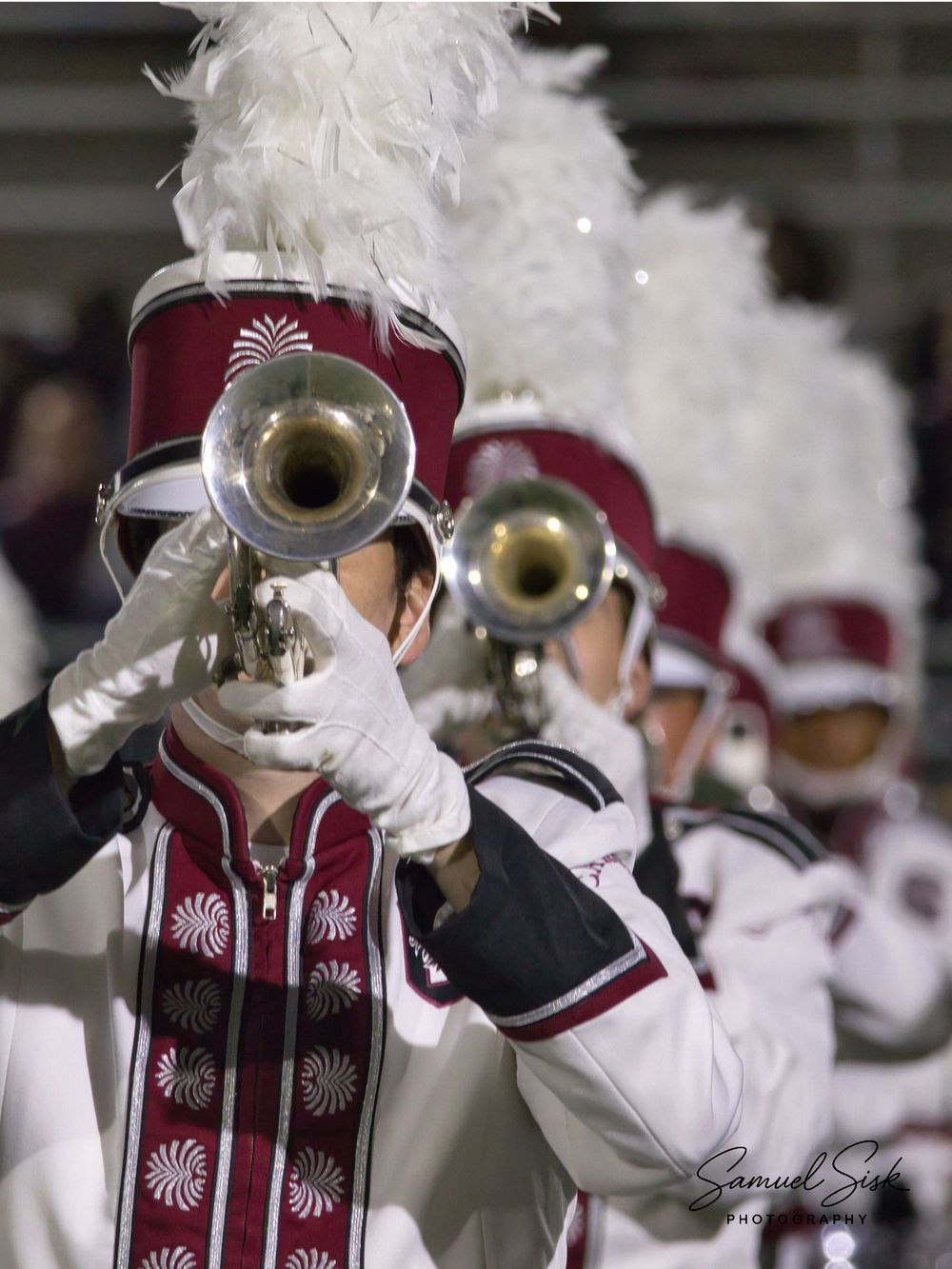 Close-up of marching band member playing silver trumpet in ornate red and white uniform.