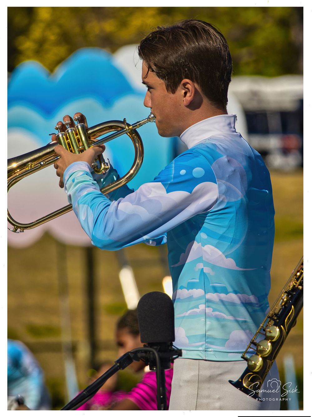 Male marching band member plays trumpet in a blue sky and clouds uniform at an outdoor competition.