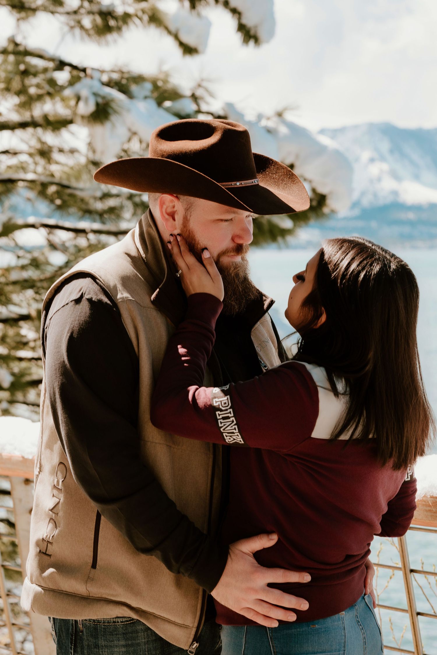 Couple sharing a romantic moment outdoors in snowy mountains, man in cowboy hat and woman in burgundy sweater.