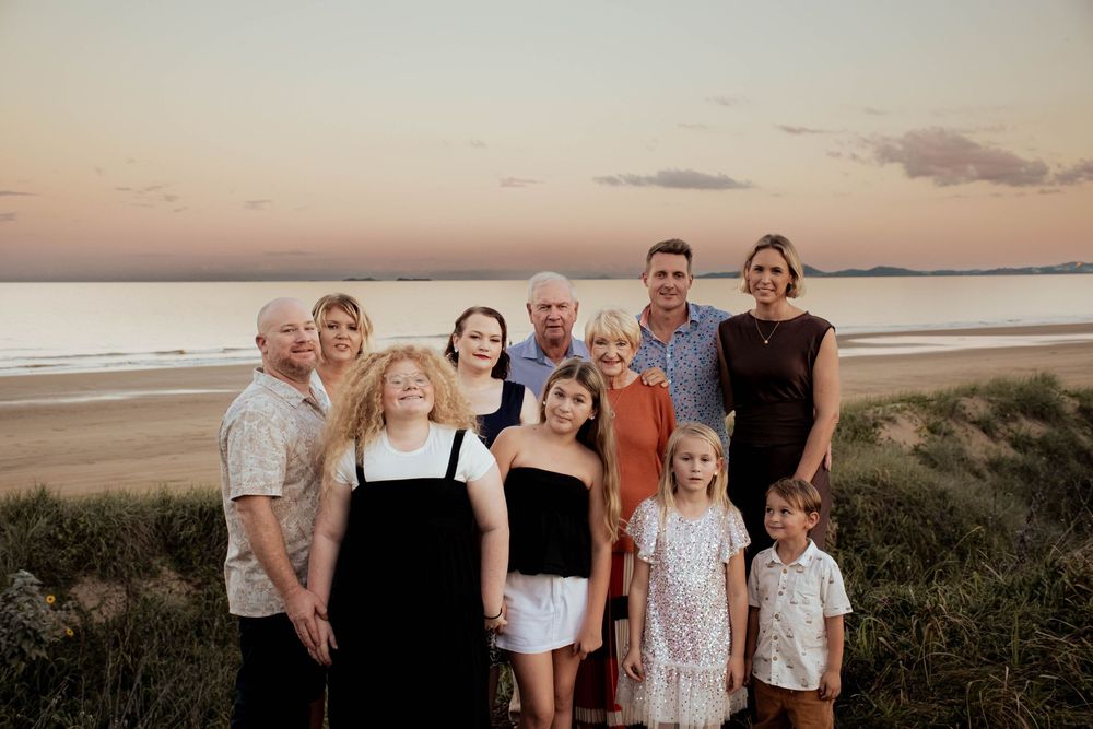 Multi-generational family portrait on sandy beach at golden sunset.