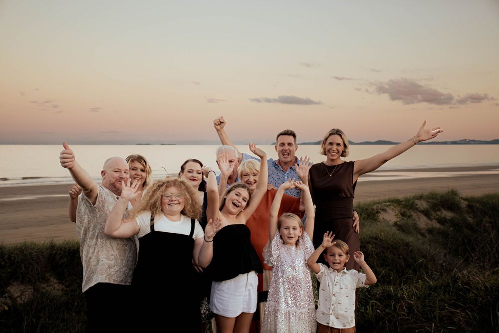 Happy family group celebrating on beach at sunset with arms raised.