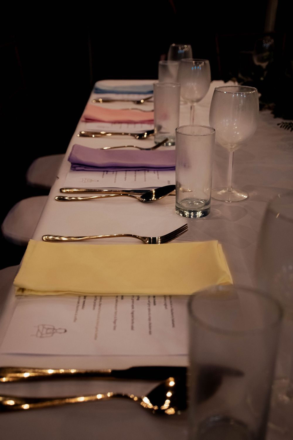 Formal dining table set with colorful pastel napkins, silverware, and crystal glasses.