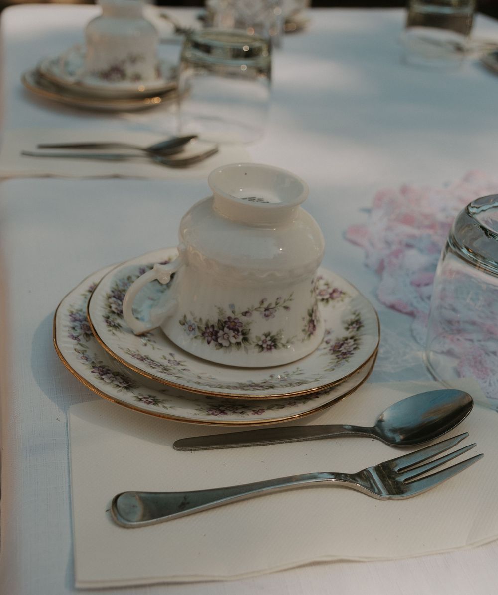 Vintage floral china place setting with teacup, plates, and silverware on white tablecloth.