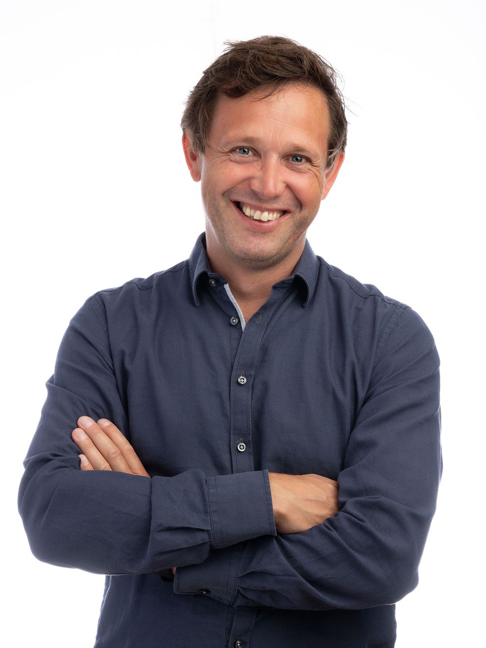 Smiling man with crossed arms wearing a navy blue shirt, posing confidently against a white background.